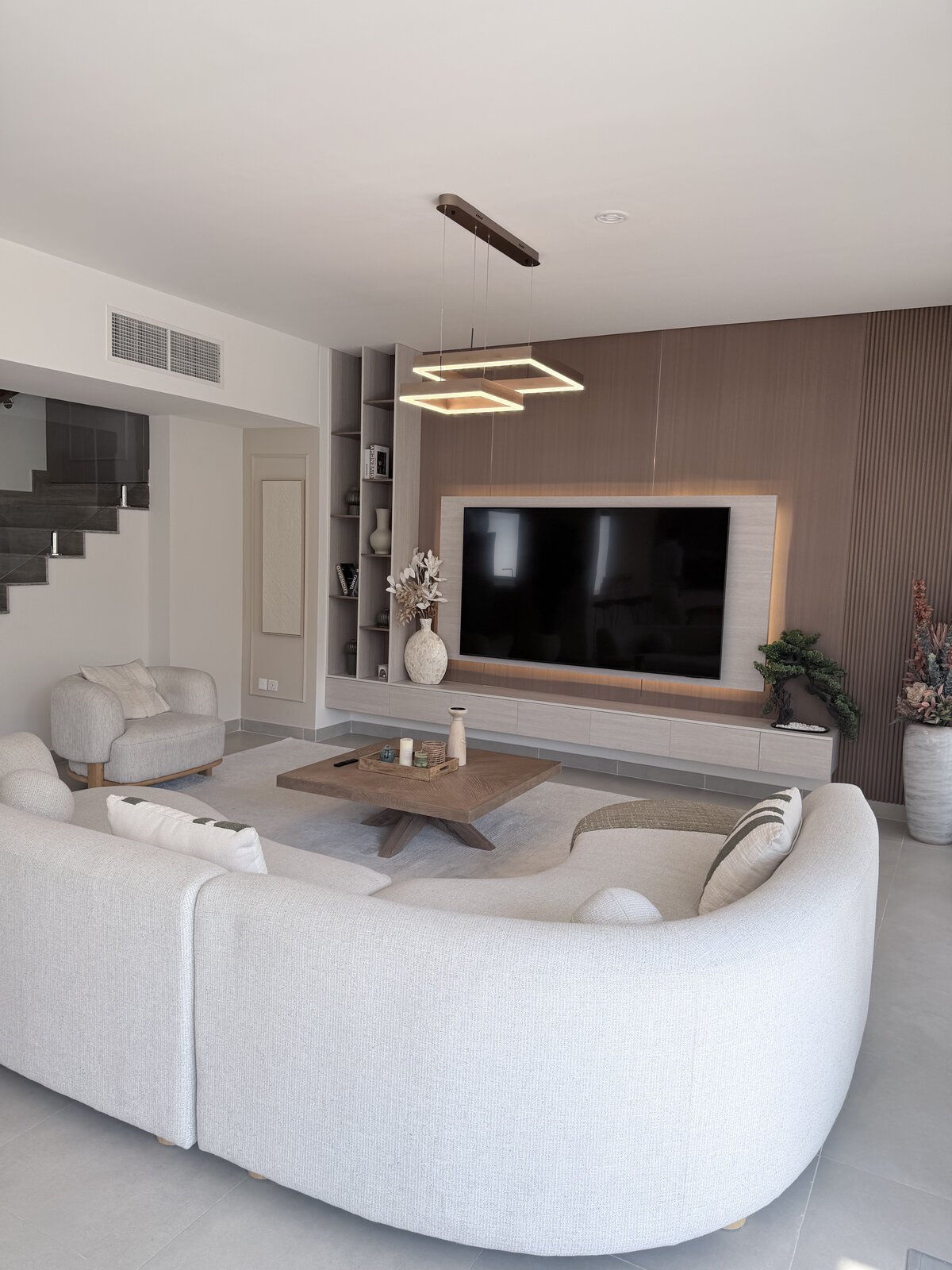 Palm Jumeirah townhouse living room after renovation — wood-paneled TV wall, curved sofa and styled furnishing